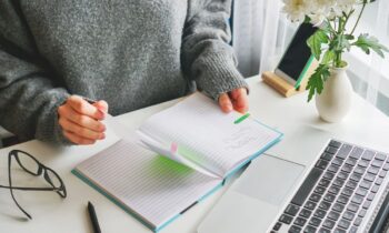 A woman working from her home office at a desk and flipping through a planner.