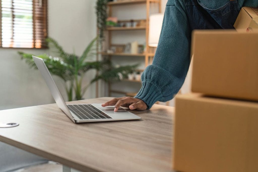 An Etsy seller using a laptop while preparing products for shipment.