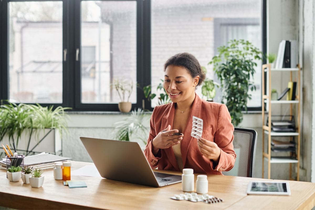 A female doctor, working from home, using a laptop to take a telehealth call and explain medication.