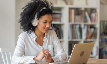 A teacher working from her home office on a laptop with books in the background.