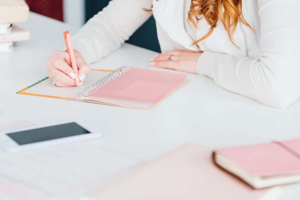 A woman working from home at a desk and writing in a notebook.