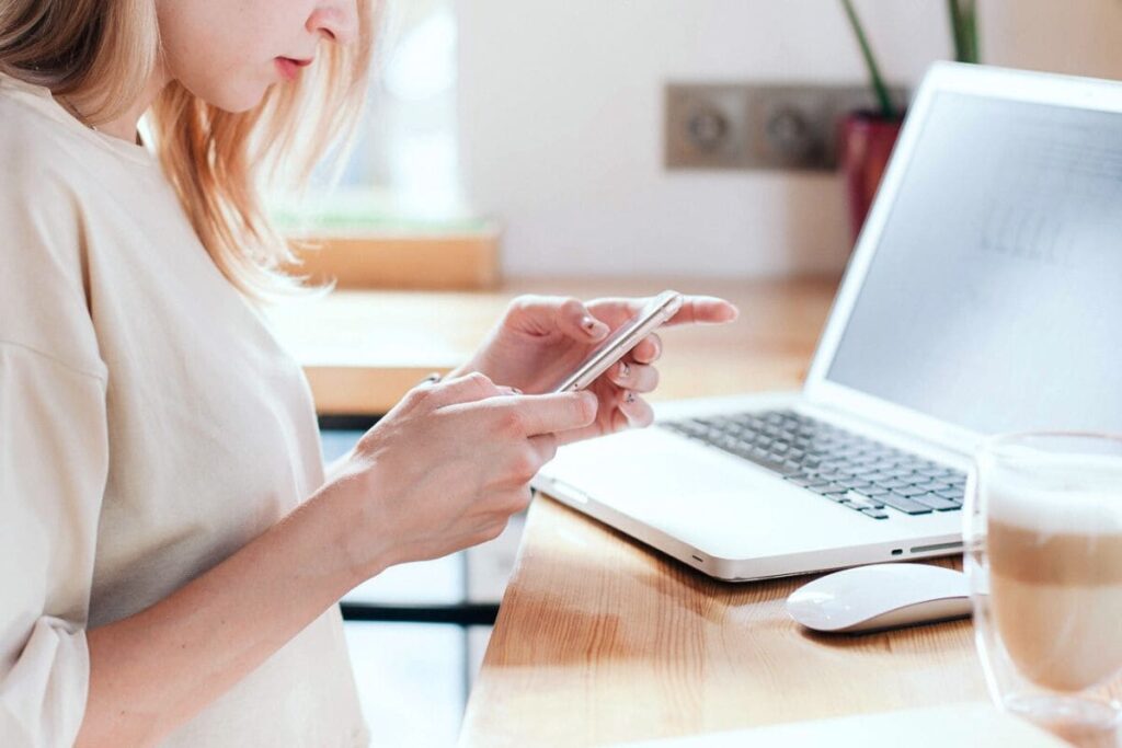 A woman working at home, sitting at a computer desk and using her phone.