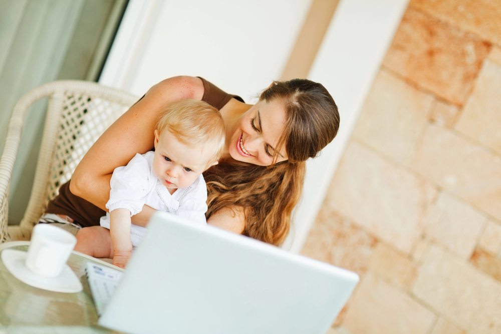 Baby sitting on mom's lap while she works on her summer work from home jobs