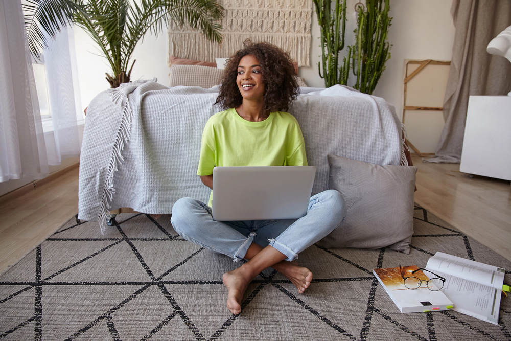 Cheerful young dark skinned woman sitting on floor using laptop and shopping online for blog post Rakuten Review