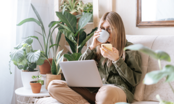 Freelance woman in glasses with mobile phone typing at laptop for her work from home job in California