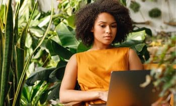 Blogger using a laptop at home office filled with plants.