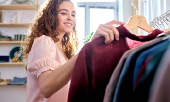 A woman standing next to a clothing rack and holding a blouse.