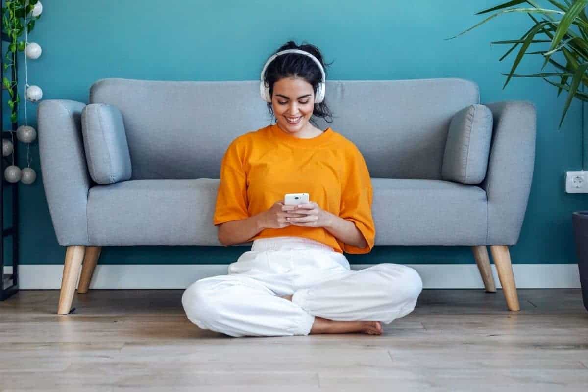 A woman sitting on the floor in her living room, wearing headphones, and getting paid to listen to music.