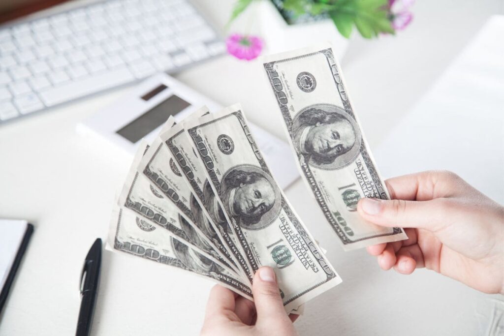 A woman counting cash at her computer desk.