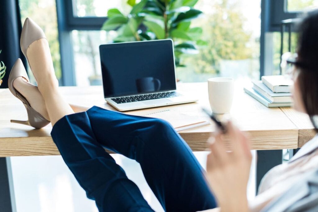 A woman working from a home office, resting her feet on her desk.