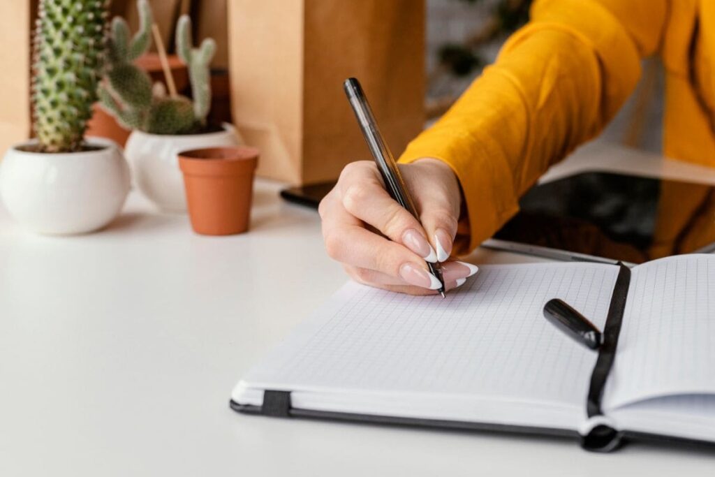 A woman working from home on a business plan, and writing in a notebook.