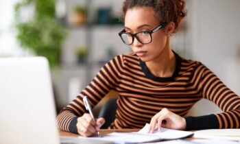 A woman working from home on a business plan, and writing in a notebook.