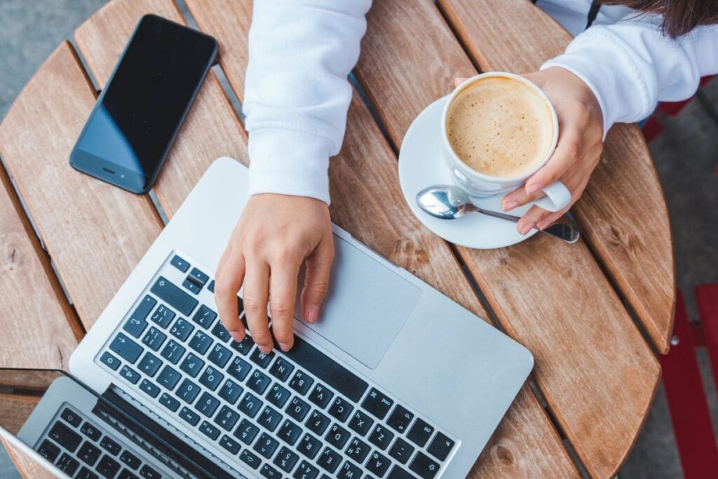 A woman taking an online survey while working on a laptop and drinking coffee at a cafe.