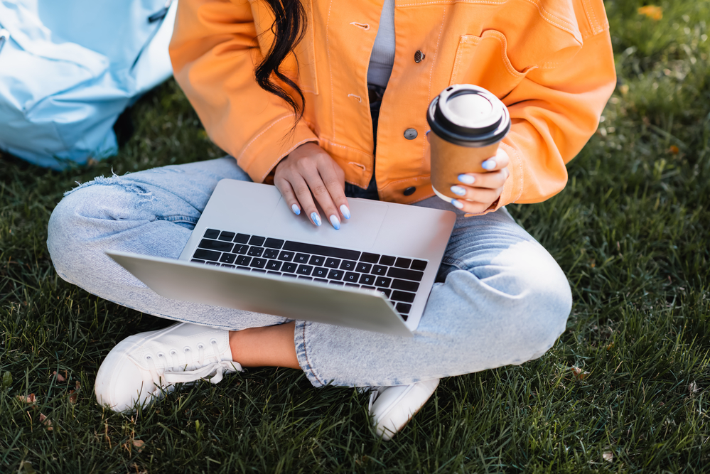 Woman in torn jeans drinking coffee taking survey with Branded Surveys on her laptop