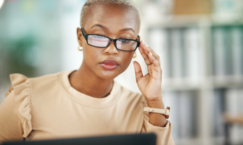 young woman wearing glasses working on a laptop proofreading documents from home