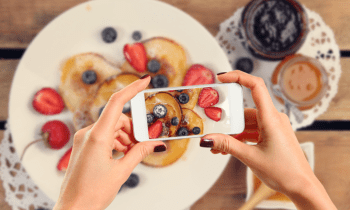 woman taking a photo with her photo of a plate of pancakes and fruit