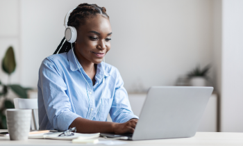 young woman with headphones on typing on her laptop computer